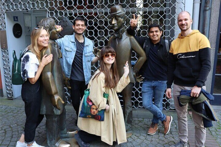 A group of people posing with a statue of a man in a hat and a fish sculpture. 1