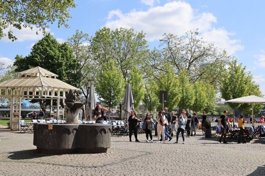 A public square with a fountain, people walking, and outdoor seating areas. 4