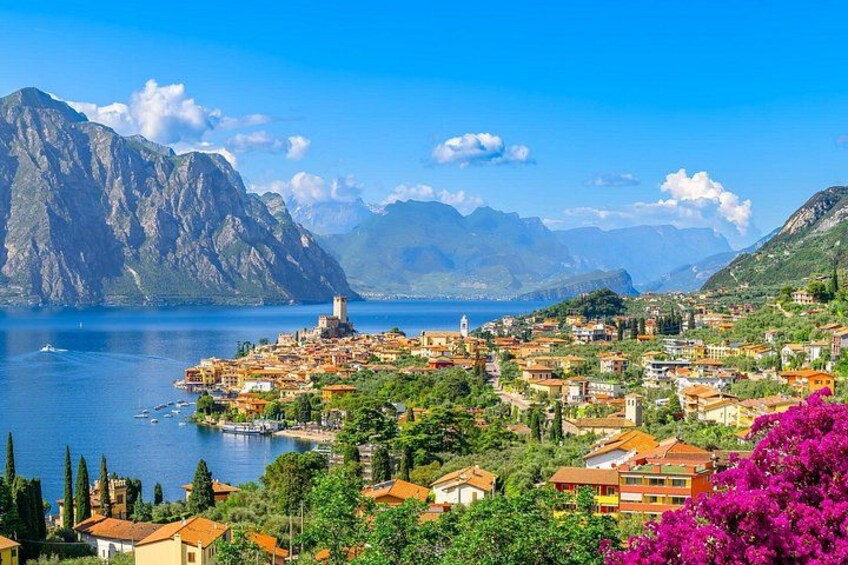 A coastal town with a prominent tower, mountains in the background, and a clear blue sea. 1
