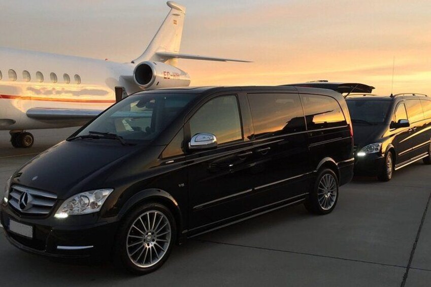 A black Mercedes-Benz van parked on a tarmac with a private jet in the background. 2