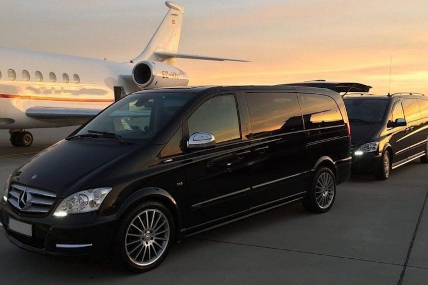 A black Mercedes-Benz van parked on a tarmac with a private jet in the background. 4