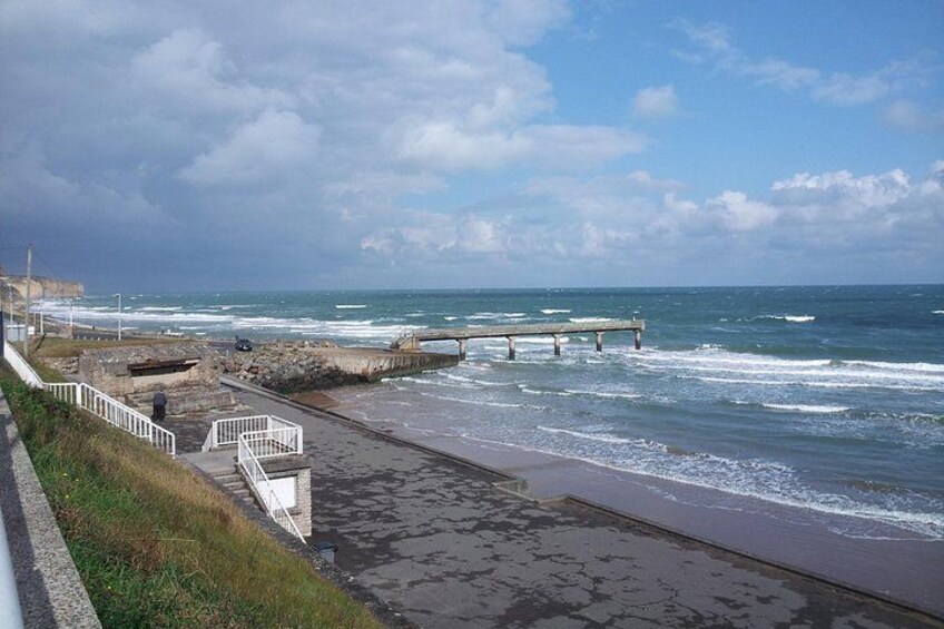 Una passeggiata costiera, una riva rocciosa, onde e un molo. 1