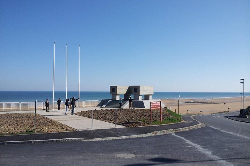 Una passeggiata costiera con una struttura moderna, cielo sereno e una spiaggia sullo sfondo. 5