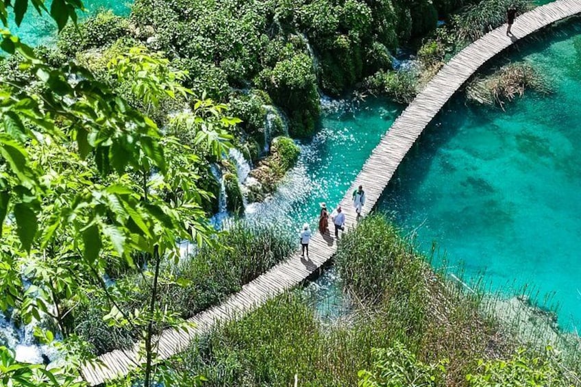 A wooden bridge over a turquoise river, surrounded by lush greenery and a waterfall. 2