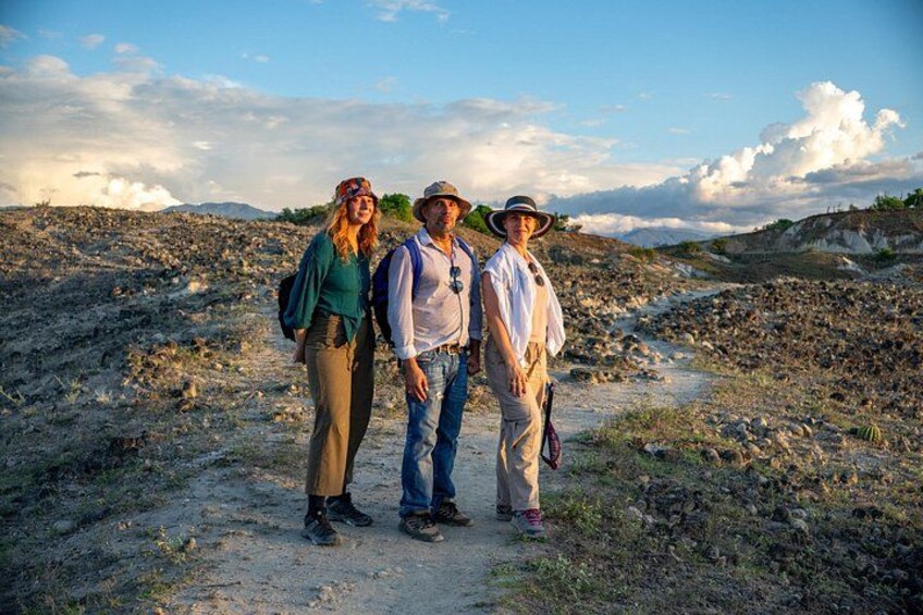 Three people standing on a dirt path in a rocky landscape with hills in the background. 2