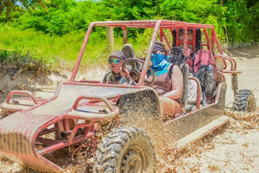 A red off-road vehicle with passengers, driving through a muddy terrain. 1