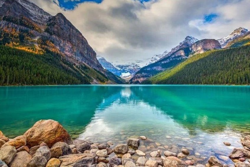 A mountain lake with clear turquoise water, surrounded by forested mountains and rocky shores. 2