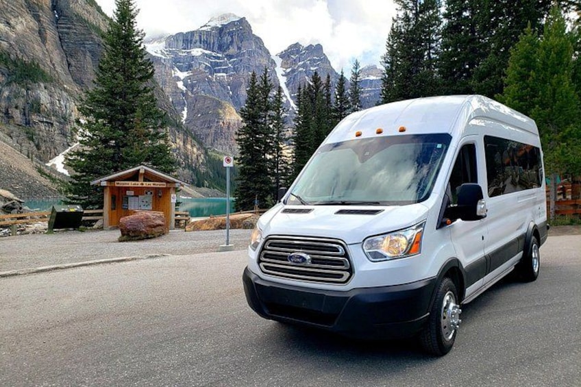 A white RV parked in a mountainous area with a small cabin and a sign in the background. 3