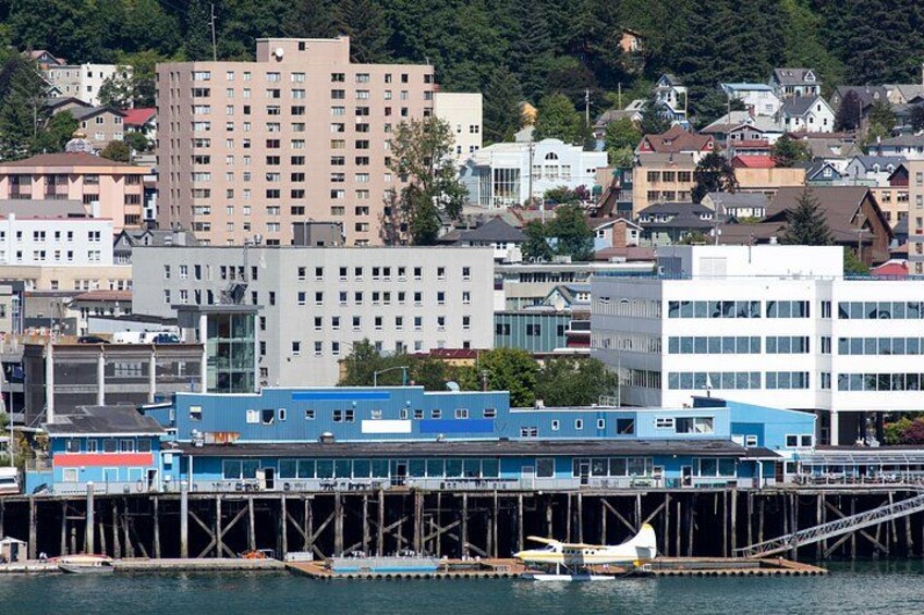 A coastal cityscape with a prominent pier, a small boat, and various buildings including a tall residential building and a modern office complex. 2