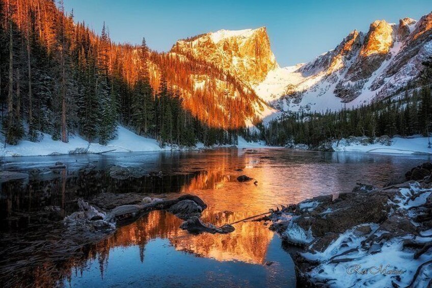 A mountain lake with reflections, snow-covered ground, and evergreen trees. 5