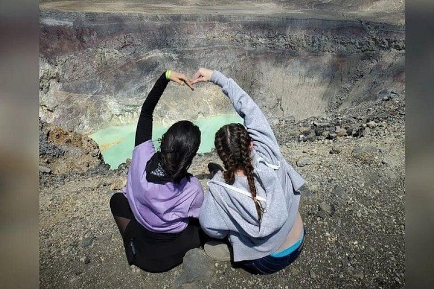 Two people sitting on the ground, one with a purple top and the other with a grey top, in front of a large open pit. 1