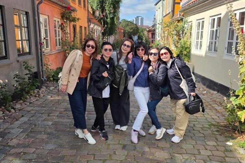 A group of people standing on a cobblestone street with buildings on either side. 1