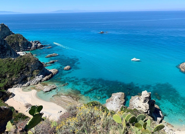 A coastal landscape with clear turquoise waters, rocky formations, and sparse vegetation. 1