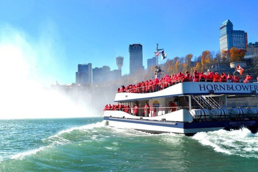 Un bateau nommé « Hornblower », transportant des passagers vêtus de vestes rouges, navigue sur une étendue d’eau, avec la silhouette d’une ville en arrière-plan. 1