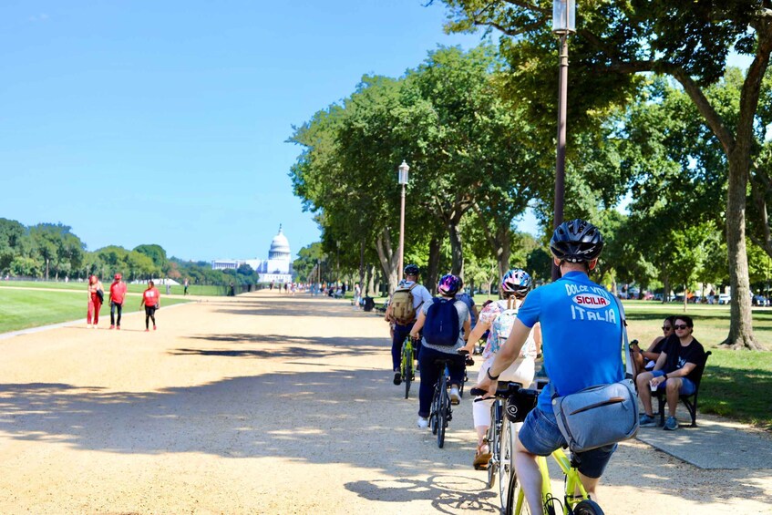 Un gruppo di ciclisti su un sentiero asfaltato, con alberi e una vista lontana di un edificio a cupola. 3