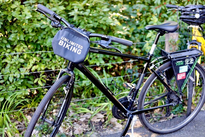 A black bicycle with a basket and a bag labeled "UNLIMITED BIKING" attached to the handlebars. 2