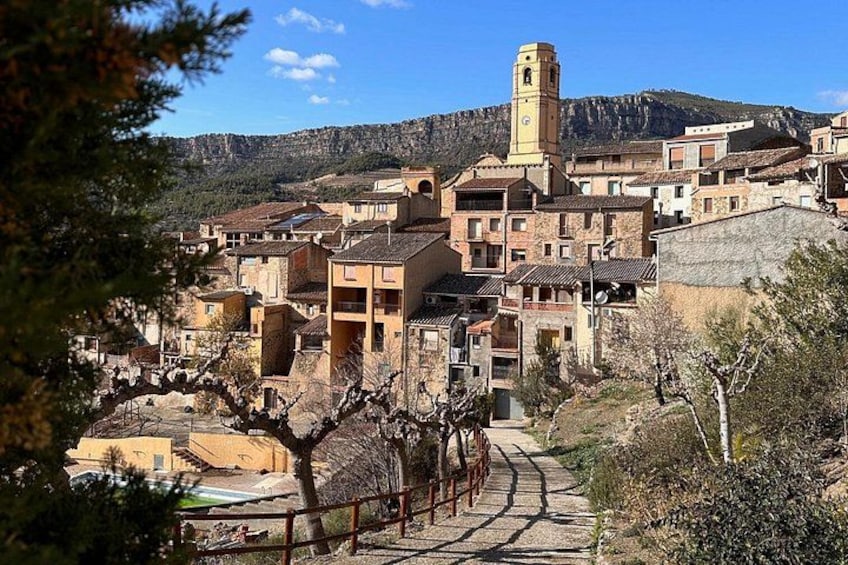 A village with stone buildings, a prominent tower, and a mountainous backdrop. 2