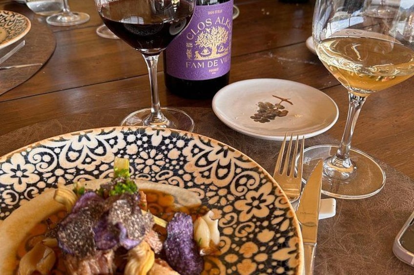 A table with a plate of food, a bottle of wine, and two glasses of wine. 3