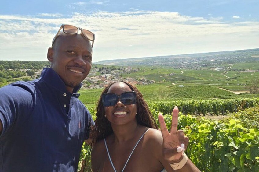 Two people taking a selfie with a vineyard and a distant town in the background. 2