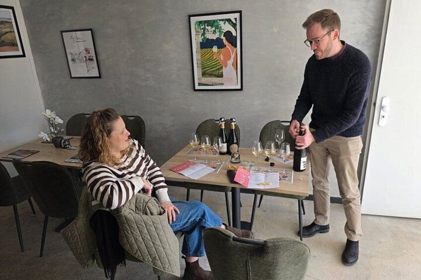 A person pouring wine into a glass, seated at a table with wine bottles and glasses. 2