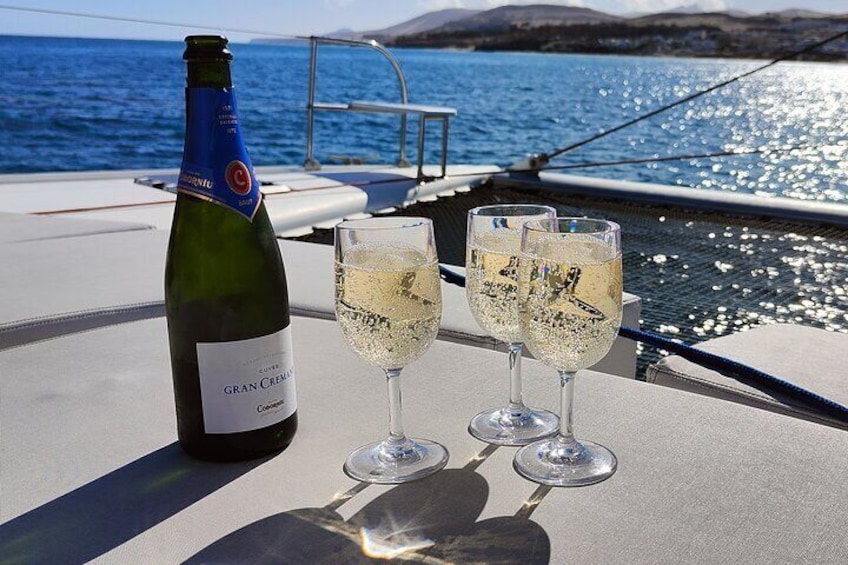 A bottle of Gran Cremalonga wine and two glasses of champagne on a boat deck with a view of the sea. 1