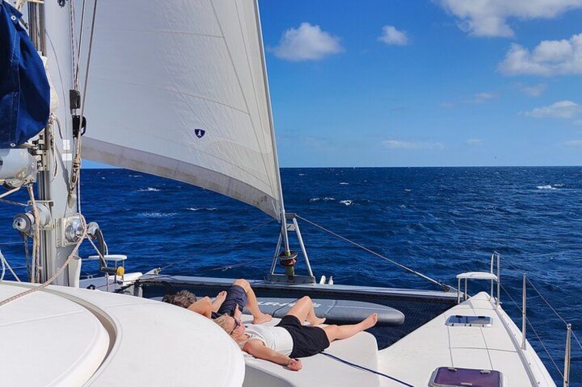 Een zeilboot met twee personen die op het dek liggen, een wit zeil en de oceaan. 2