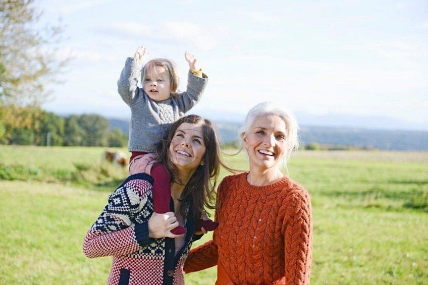 Une personne portant un enfant sur ses épaules, une autre personne se tenant à côté d’elle, et un champ herbeux avec des arbres en arrière-plan. 4