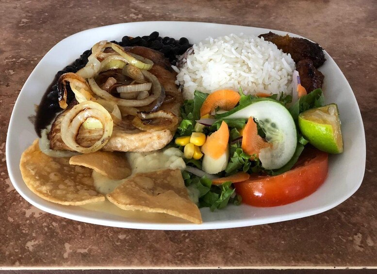 A plate of food with rice, black beans, grilled meat, onions, salad, corn, and a tortilla. 5
