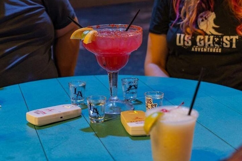 Een tafel met een groot rood cocktaildrankje, shot glaasjes en een klein apparaat. 2
