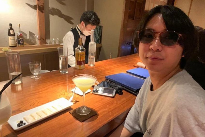 A bar setting with a person seated, a bar counter, glasses, bottles, and a menu. 3