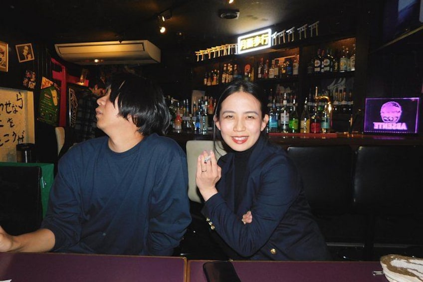 Two people seated at a bar with a neon sign in the background. 5