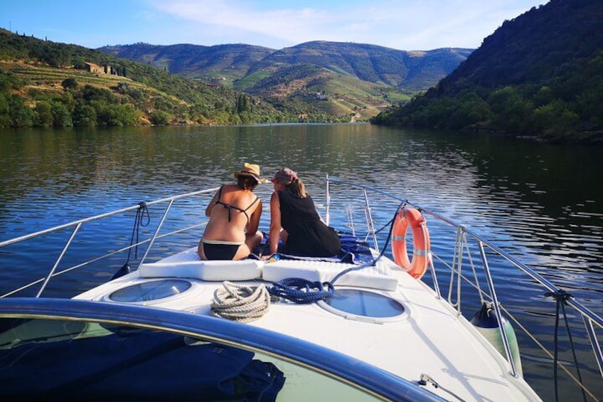 A boat on a river with two people on deck, surrounded by green hills and a clear sky. 4