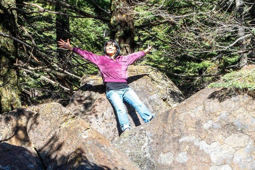 A person sitting on a rock with arms outstretched in a forested area. 5