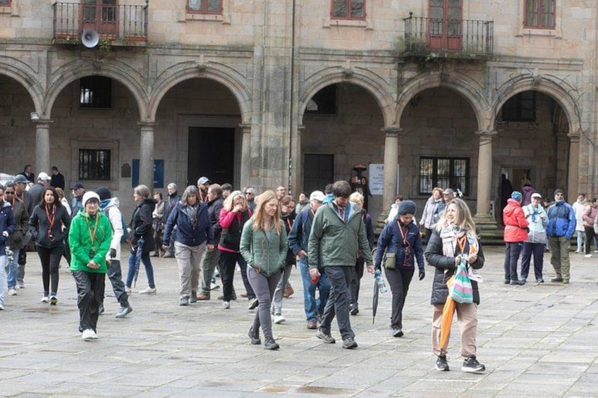 A crowded square with people walking, a historic building with arches, and a stone pavement. 2