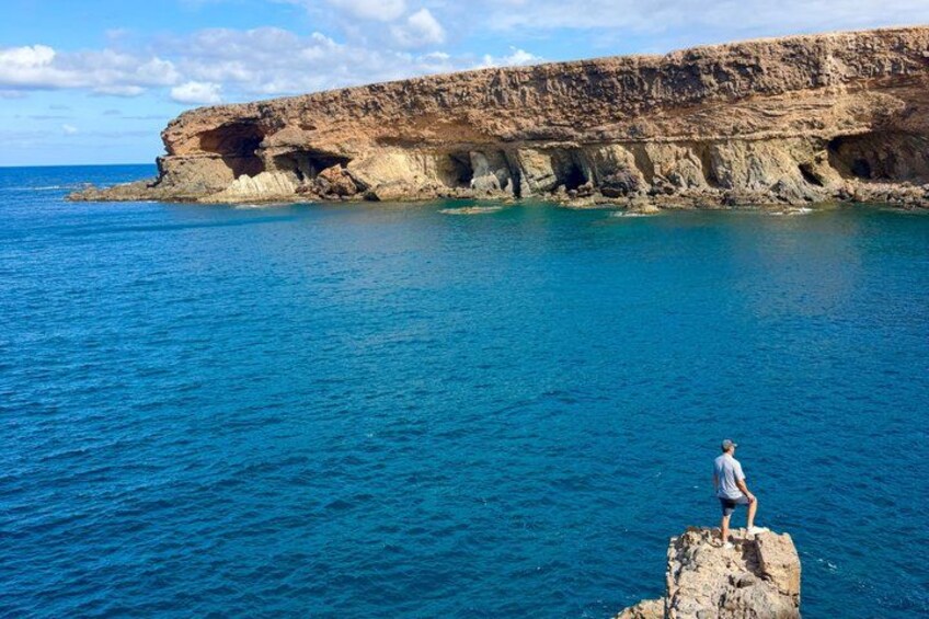 A person standing on a rock by the sea with cliffs in the background. 2