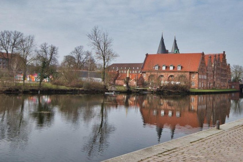 A calm river reflecting a historic building with a red roof and two spires. 4