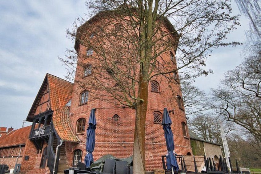 A red brick tower with a tree in front, a covered area with umbrellas, and a building with a sloped roof. 2