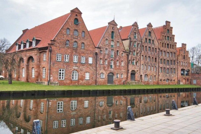 A large brick building with a red roof, a reflective water body in front, and a paved walkway. 3