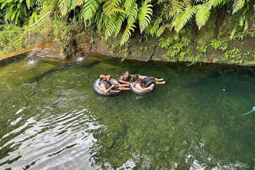People floating on tubes in a clear water body surrounded by greenery. 2