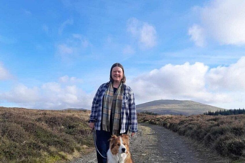 A person walking a dog on a dirt path with a hilly landscape in the background. 1