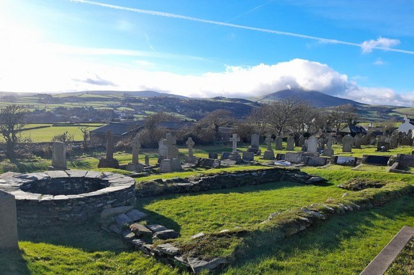 A cemetery with stone crosses and a circular stone structure, surrounded by green fields and hills. 2
