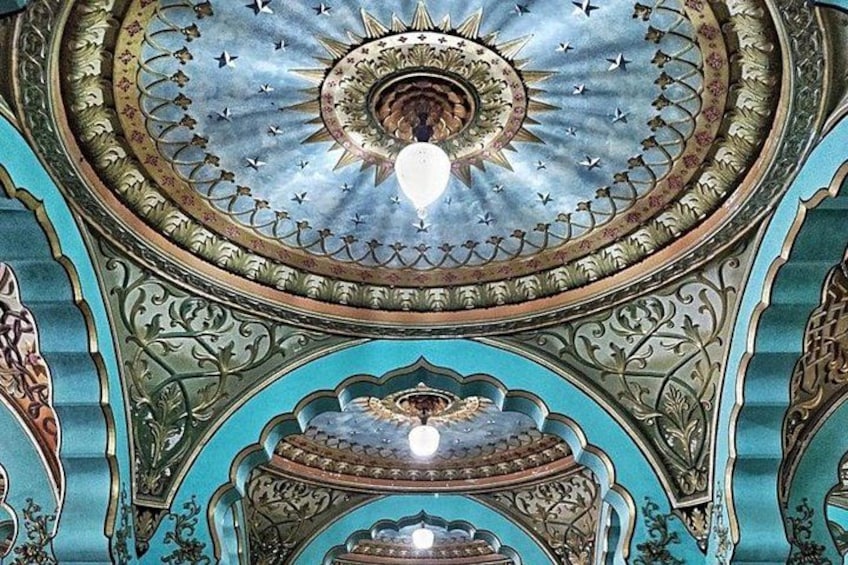 A detailed ceiling with a central sun motif, surrounded by ornate patterns and a blue sky design. 3