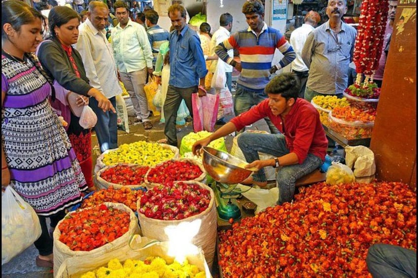 A bustling market with people shopping and a vendor sorting flowers. 4