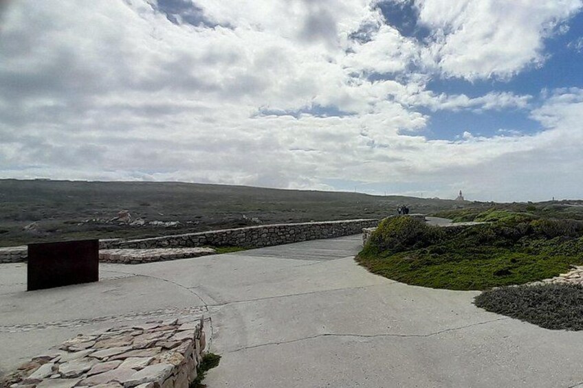 A coastal walkway with a stone wall, grassy areas, and a distant lighthouse. 3