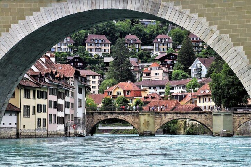 A stone bridge over a river with houses on a hillside in the background. 4