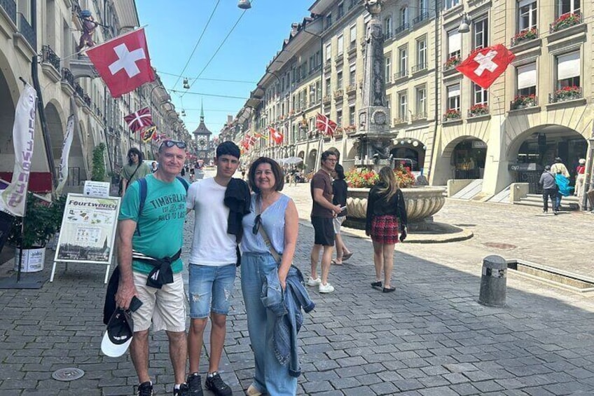 A group of people posing in a city square with Swiss flags and a fountain. 2