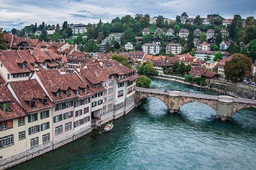 A river with a stone bridge, buildings with red-tiled roofs, and a hilly background. 4
