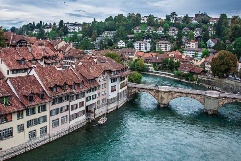 A river with a stone bridge, buildings with red-tiled roofs, and a hilly background. 2