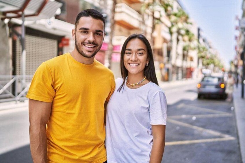 Two people standing on a city street with buildings and a car in the background. 3