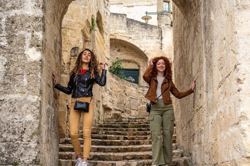 Two people standing in a narrow stone corridor with steps leading up to an arched doorway. 1
